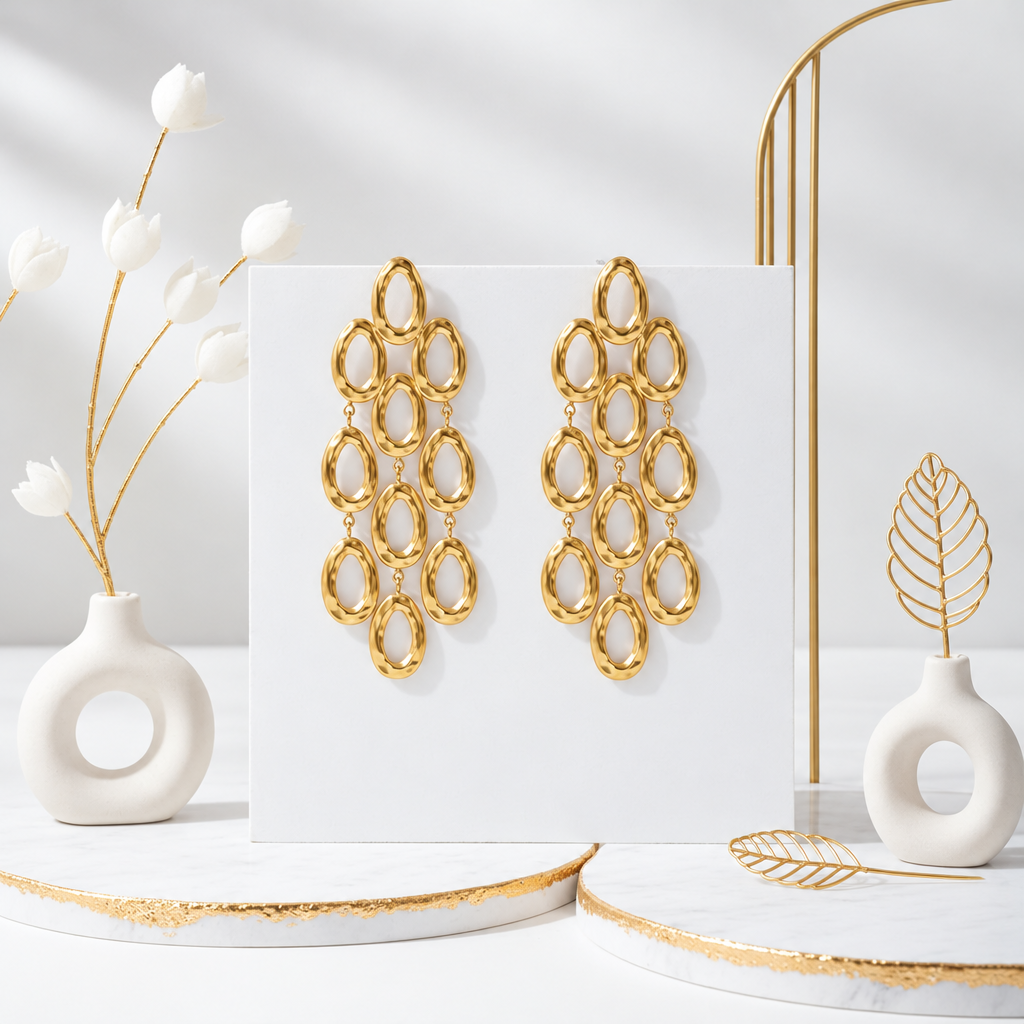 18k PVD Gold chandelier earrings with cascading oval rings displayed on a white panel amid ceramic vases and gold accents