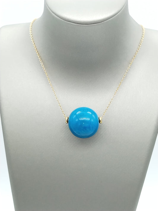 Turquoise tagua bead pendant on gold chain necklace against white background