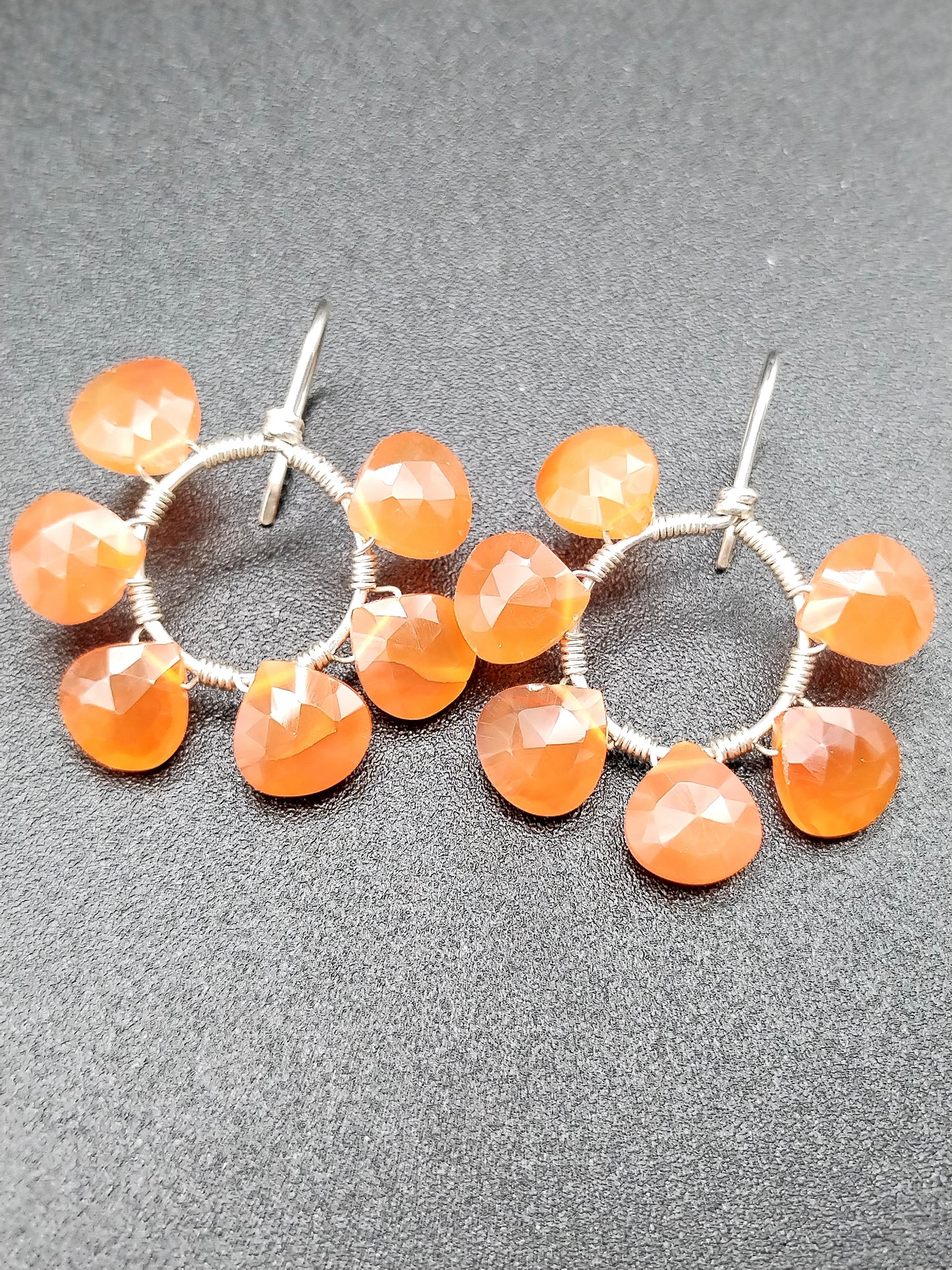 Woman wearing carnelian open hoop hook earrings showing natural orange gemstone