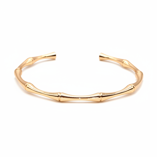 18k gold bamboo cuff bracelet displayed on white and gold surface with natural lighting