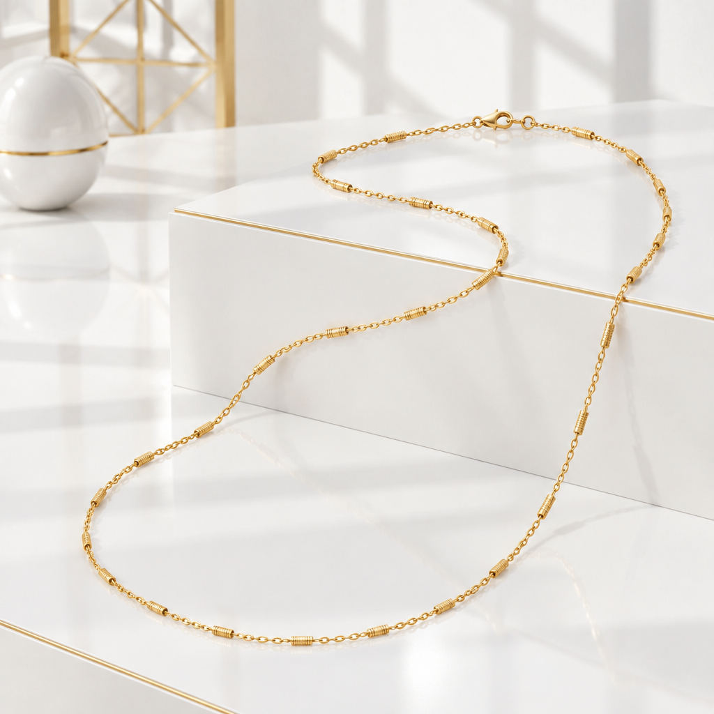 Dainty gold bar station chain draped over a white podium with a fine gold edge
