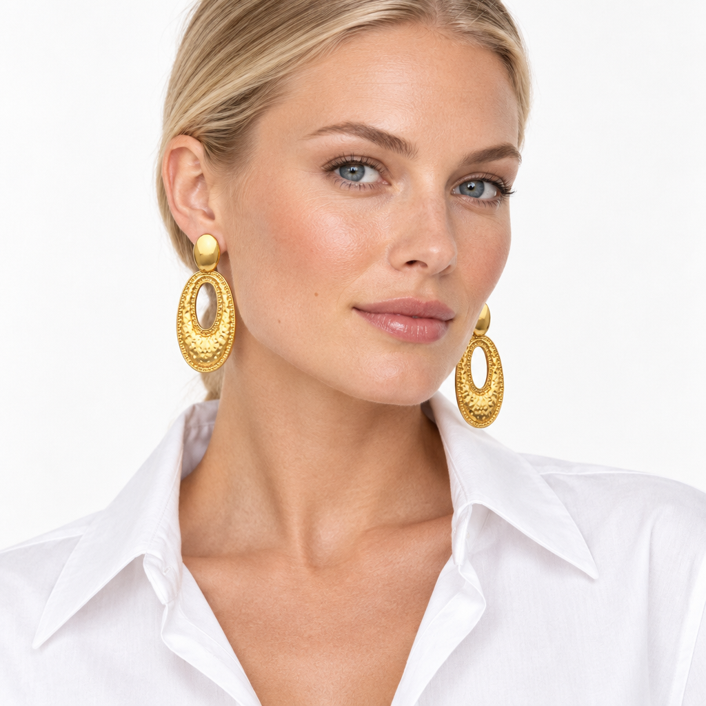 Model wearing long hammered oval drop earrings in 18k PVD Gold with an open collar white shirt