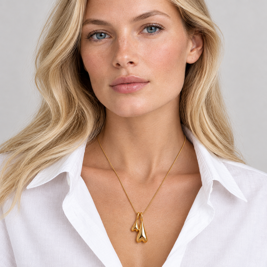 Delicate gold necklace with two inverted heart charms worn over an open collar
