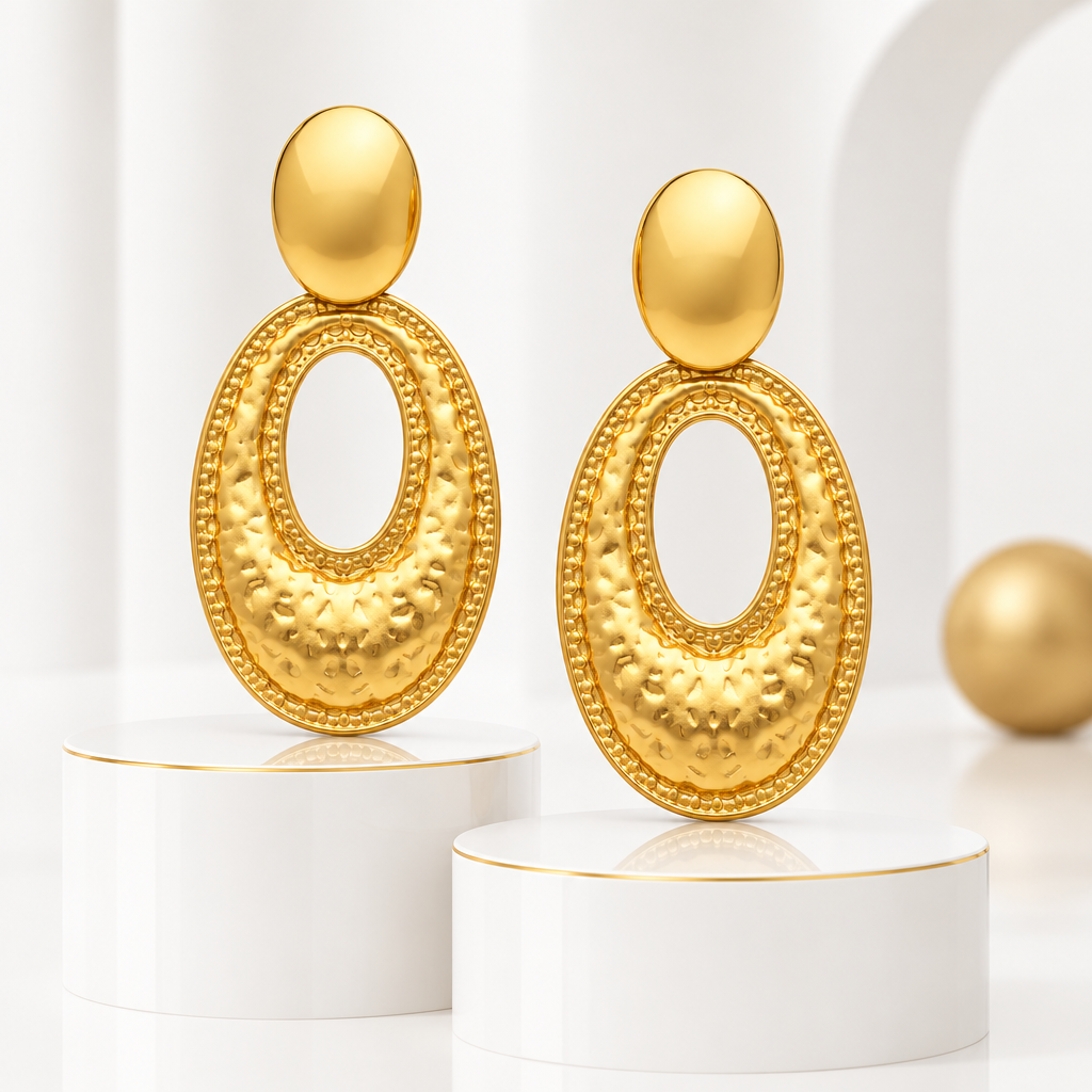 Hammered oval drop earrings in 18k PVD Gold on white podiums with fine gold edges and a matte gold sphere in the background