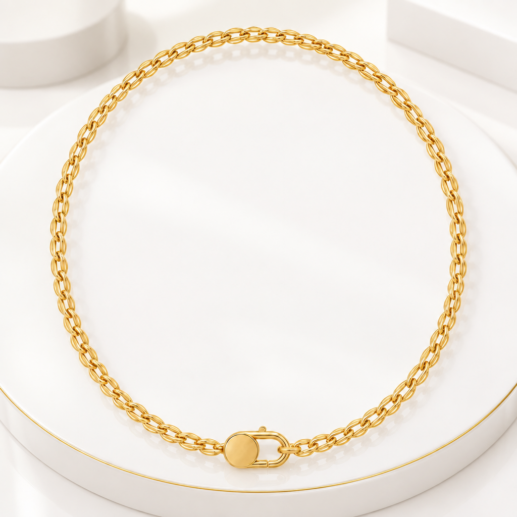 18k Gold Plated link necklace with an oval clasp, draped over a white pedestal with fine gold edges 