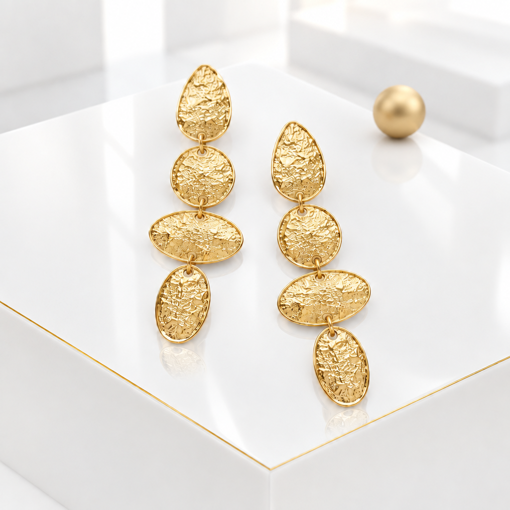 Hammered dangle earrings in 18k Gold Plated on a glossy white podium with a matte gold sphere in the background