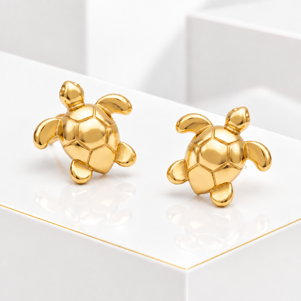 Polished turtle stud earrings in 18k Gold Plated arranged diagonally on a white podium with a fine gold edge