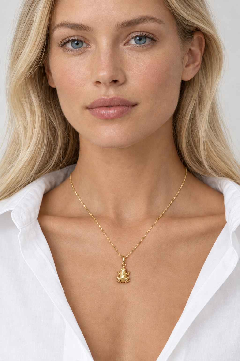 Blonde model wearing a dainty gold frog necklace with an open white shirt, lucky frog pendant resting on her chest

