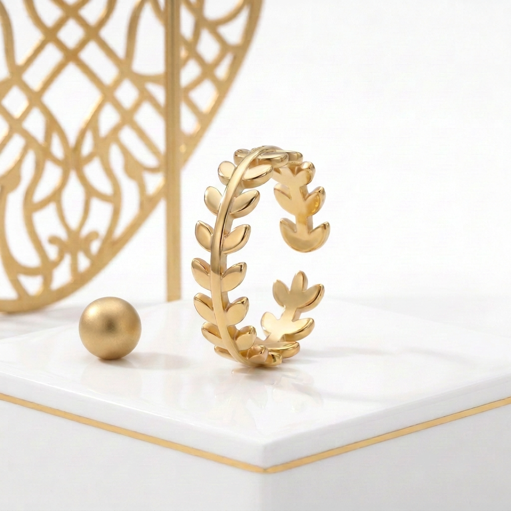 18k Gold Plated leaf ring standing on a white pedestal with a fine gold edge beside a matte gold sphere