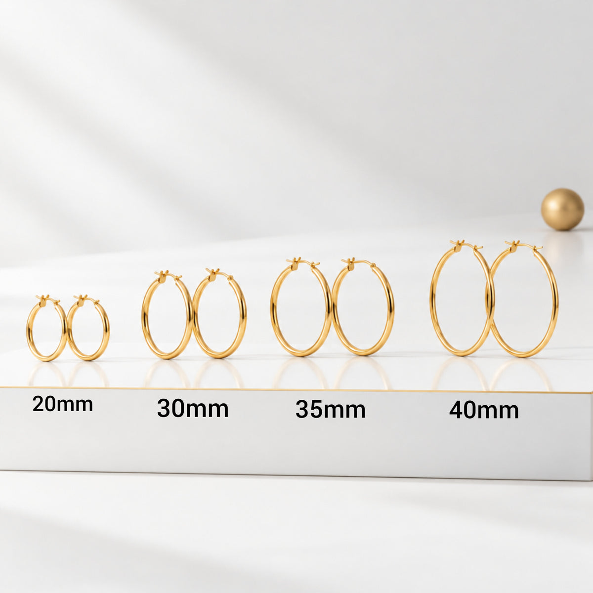 Four pairs of classic 18k gold plated hoop earrings in 20, 30, 35 and 40mm sizes, arranged from smallest to largest on a white podium
